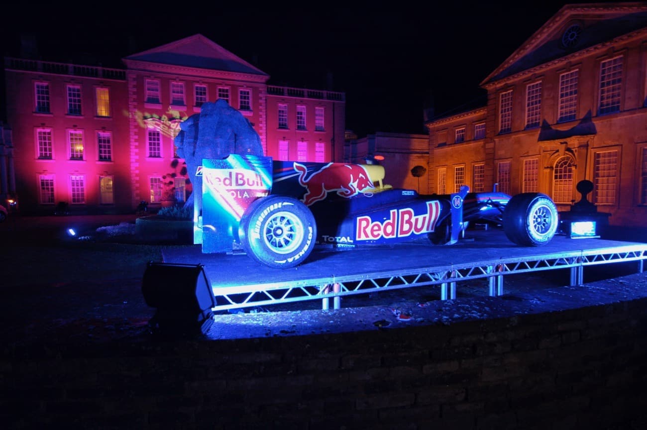Red Bull F1 Car on stage outside Aynho House at night floodlit with coloured lights