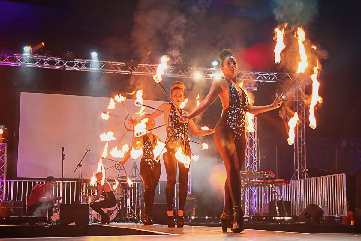 4 girls walk down a stage with fire sticks in their hands. 