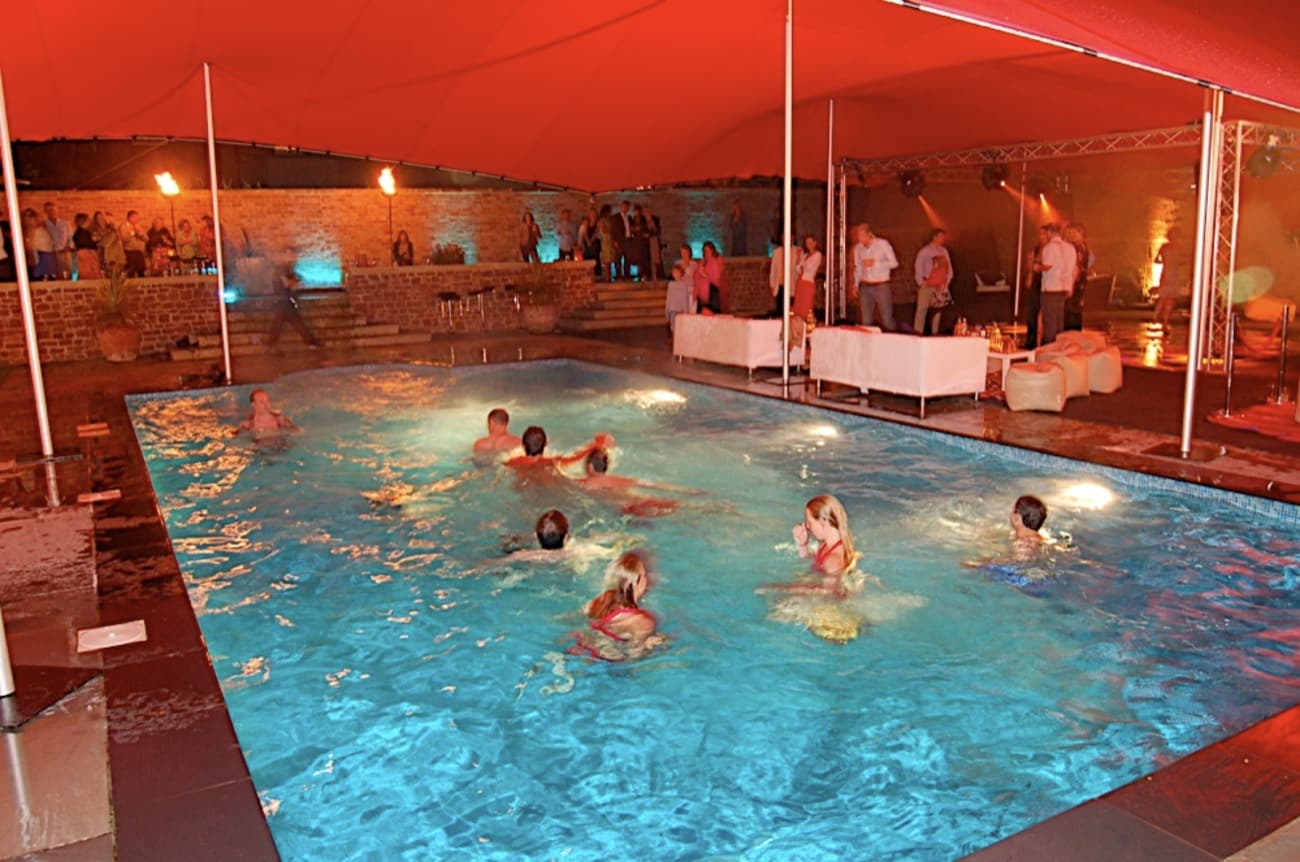 Guests jumping into a swimming pool at a pool party under a stretch tent