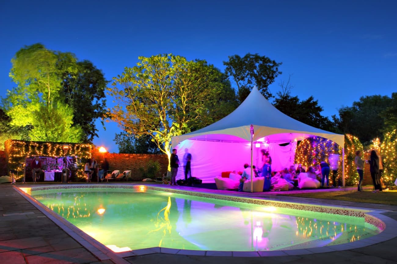 Pagoda marquee next to a swimming pool for a party at dusk lit with coloured tree lights