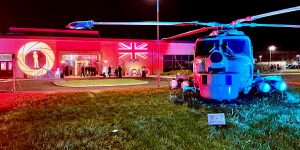 IMG_9896 The exterior of Royal Naval Air Station Yeovilton with James Bond themed lighting projected onto the front of the building. There is a helicopter in front of the building which is lit in blue.
