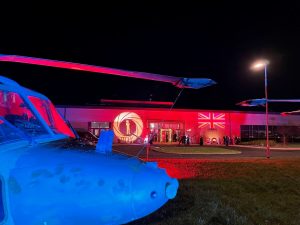 IMG_9898 The exterior of Royal Naval Air Station Yeovilton with James Bond themed lighting projected onto the front of the building. There is a helicopter in front of the building which is lit in blue.