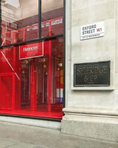 The outside of the corner shop at Selfridges, Oxford Street. Through the window you can see it is set up like a basketball court to personalise NBA jerseys for Hennessy.