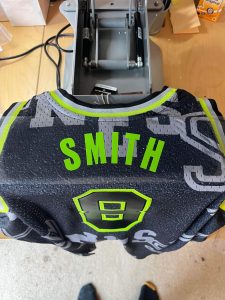 An NBA basketball jersey on a heat press, personalised with the word "Smith."