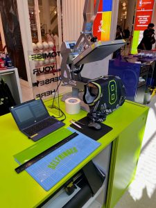 A desk with a heat press and laptop set up to personalise NBA jerseys for Hennessy.