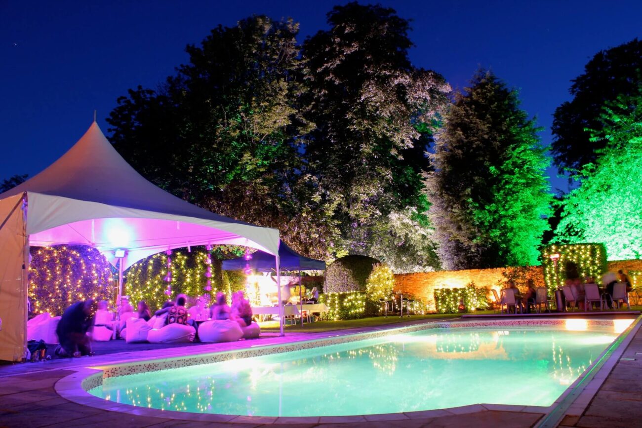 Pagoda Marquee next to a swimming pool at night. All the surrounding trees are lit up